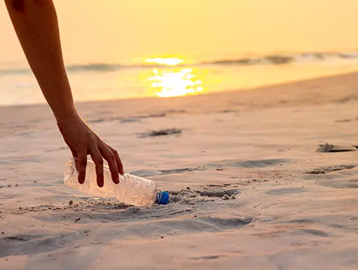 An image of a person picking up a plastic water bottle from a beach